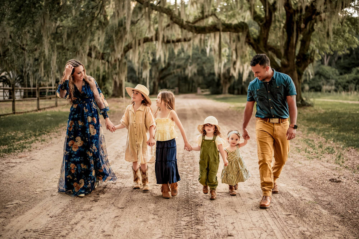 The Herndon family walking hand in hand down a dirt lane under live oaks hung with Spanish moss